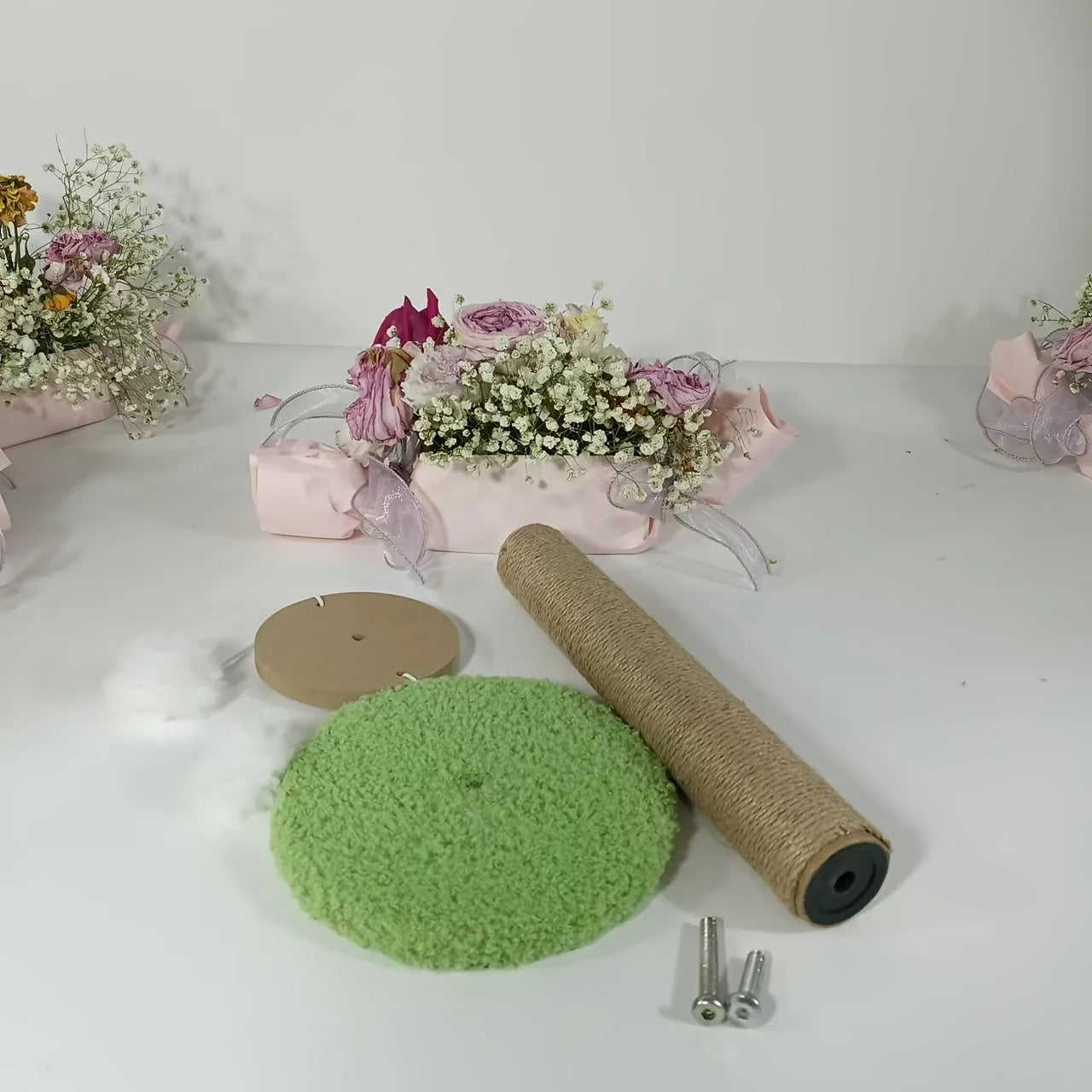 Disassembled parts of a cat condo scratching post including a green base, scratching column, screws, and floral decor in the background.