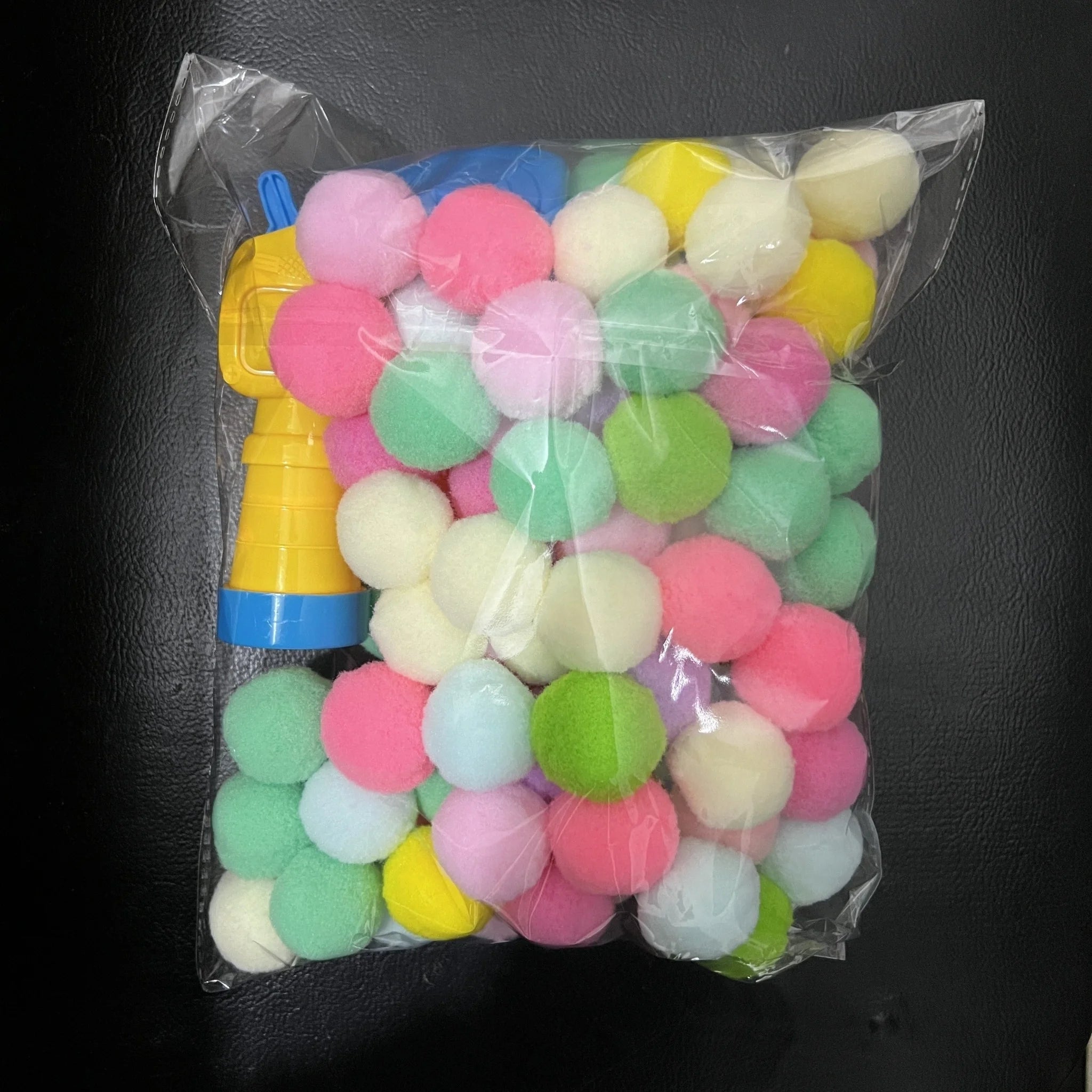 Clear bag showing a full pack of colorful pom-poms and the launcher from the cat toys for kittens set.
