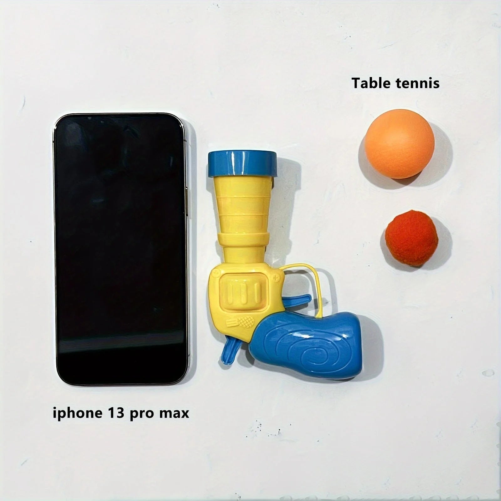 Size comparison between the launcher, a pom-pom, a table tennis ball, and an iPhone in the cat toys for kittens set.