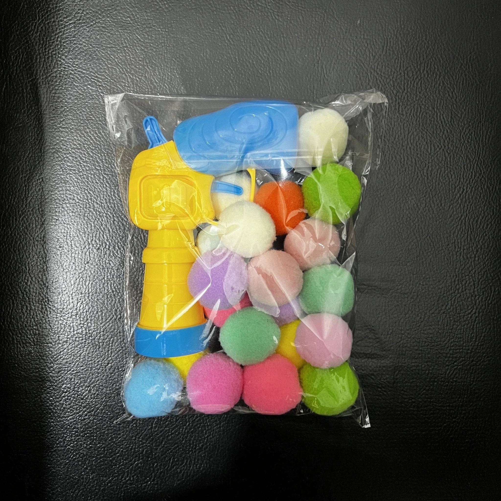 Clear bag showing a small pack of colorful pom-poms and the launcher from the cat toys for kittens set.