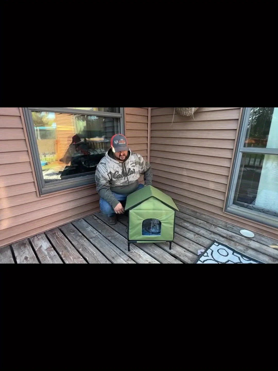 A man assembling a heated outdoor house for cats on a wooden patio.