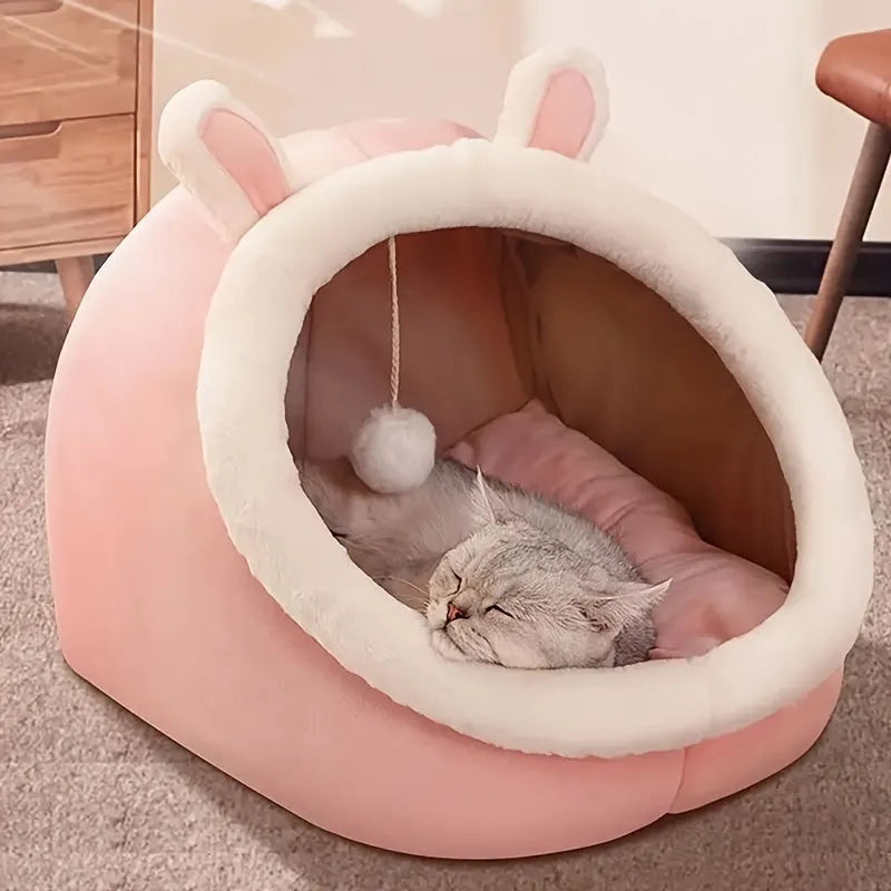 A cozy pink enclosed cat bed with bunny ears and a dangling toy ball for playful cats.