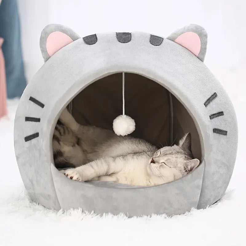 Relaxed cat enjoying the warmth inside a stylish cat bed warmer with a playful hanging plush ball