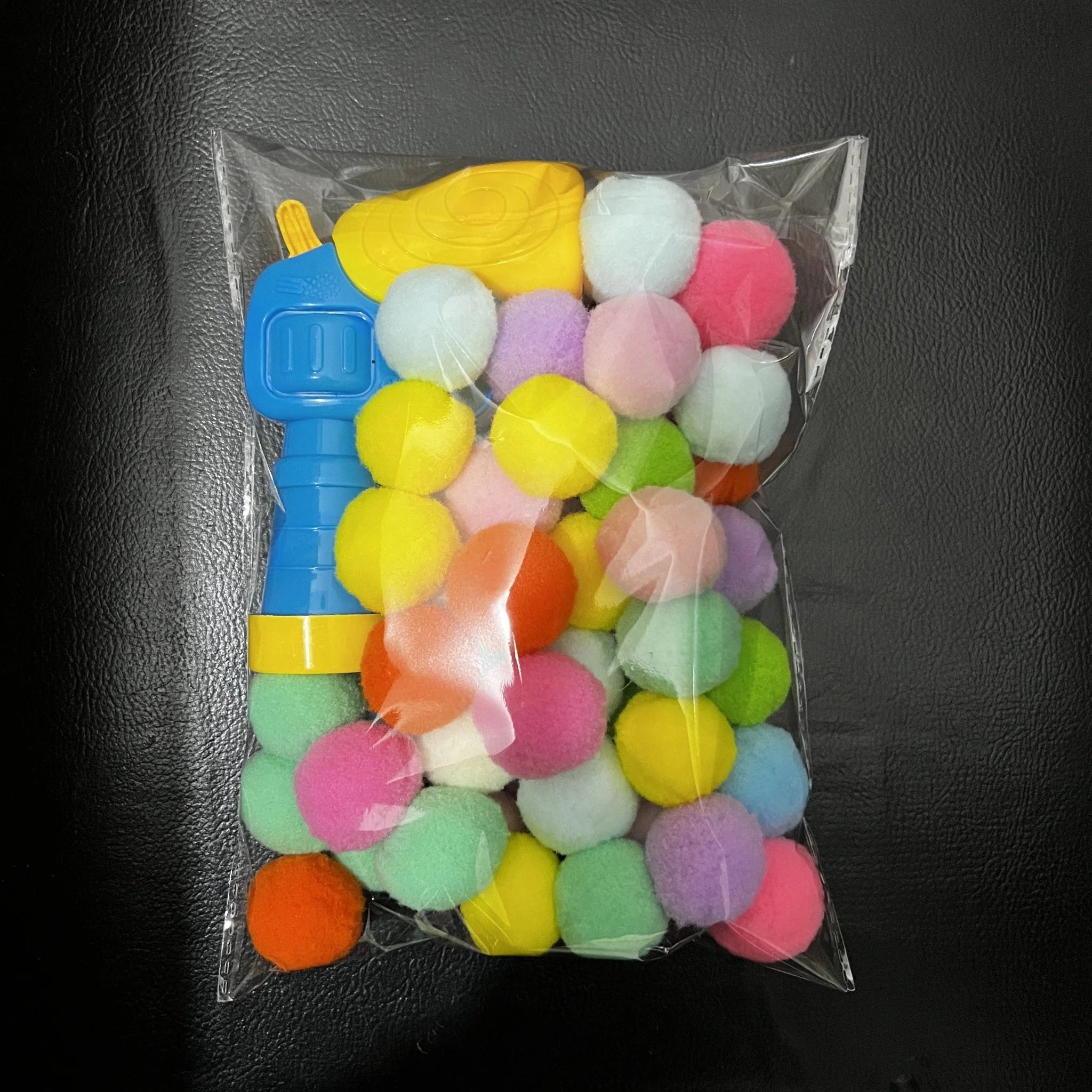 Clear bag showing a full pack of colorful pom-poms and the launcher from the cat toys for kittens set.