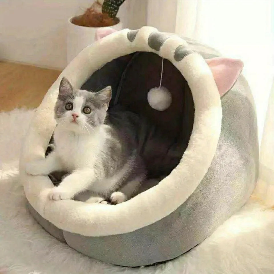 A covered cat bed with soft plush material, a spacious interior, and a hanging pom-pom toy for cats' entertainment.