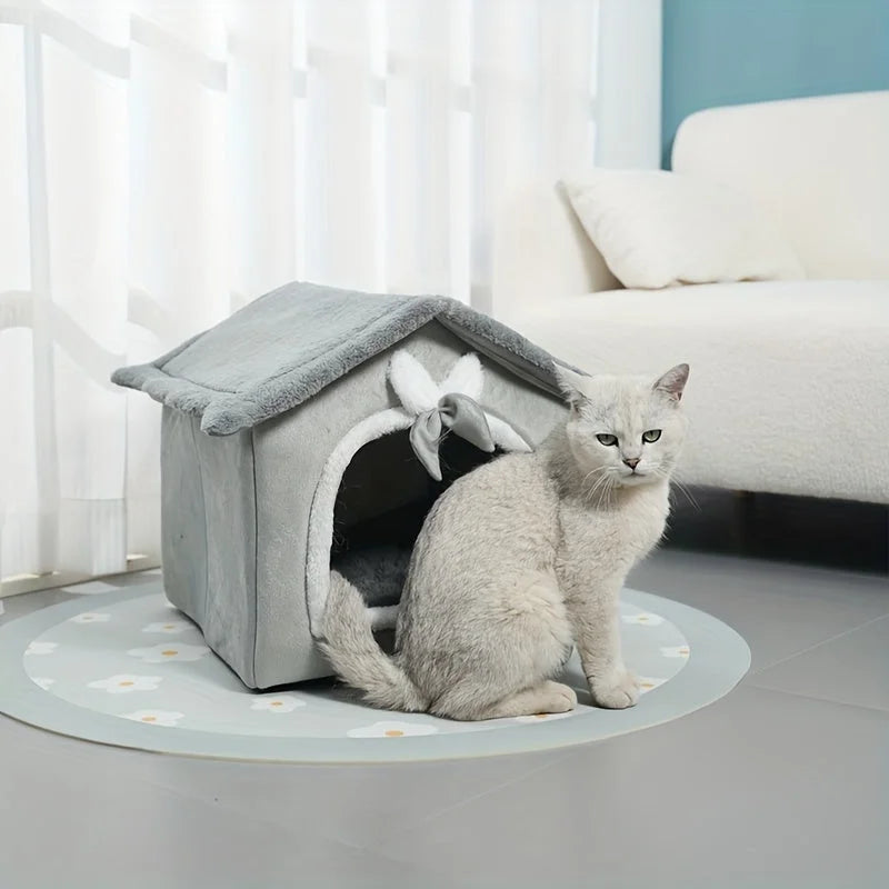 Indoor heated cat house with a cozy gray design and a cat sitting beside it.