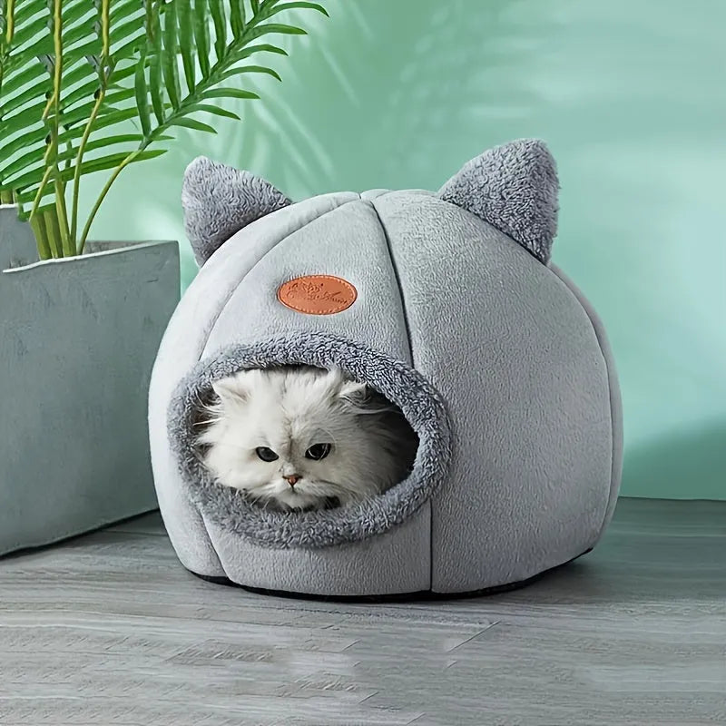 A modern and chic indoor heated cat bed in a light gray finish, placed near indoor plants.