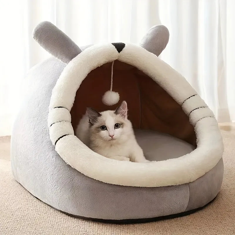 A rabbit-shaped covered cat bed in gray and white, featuring a hanging toy for playful pets.