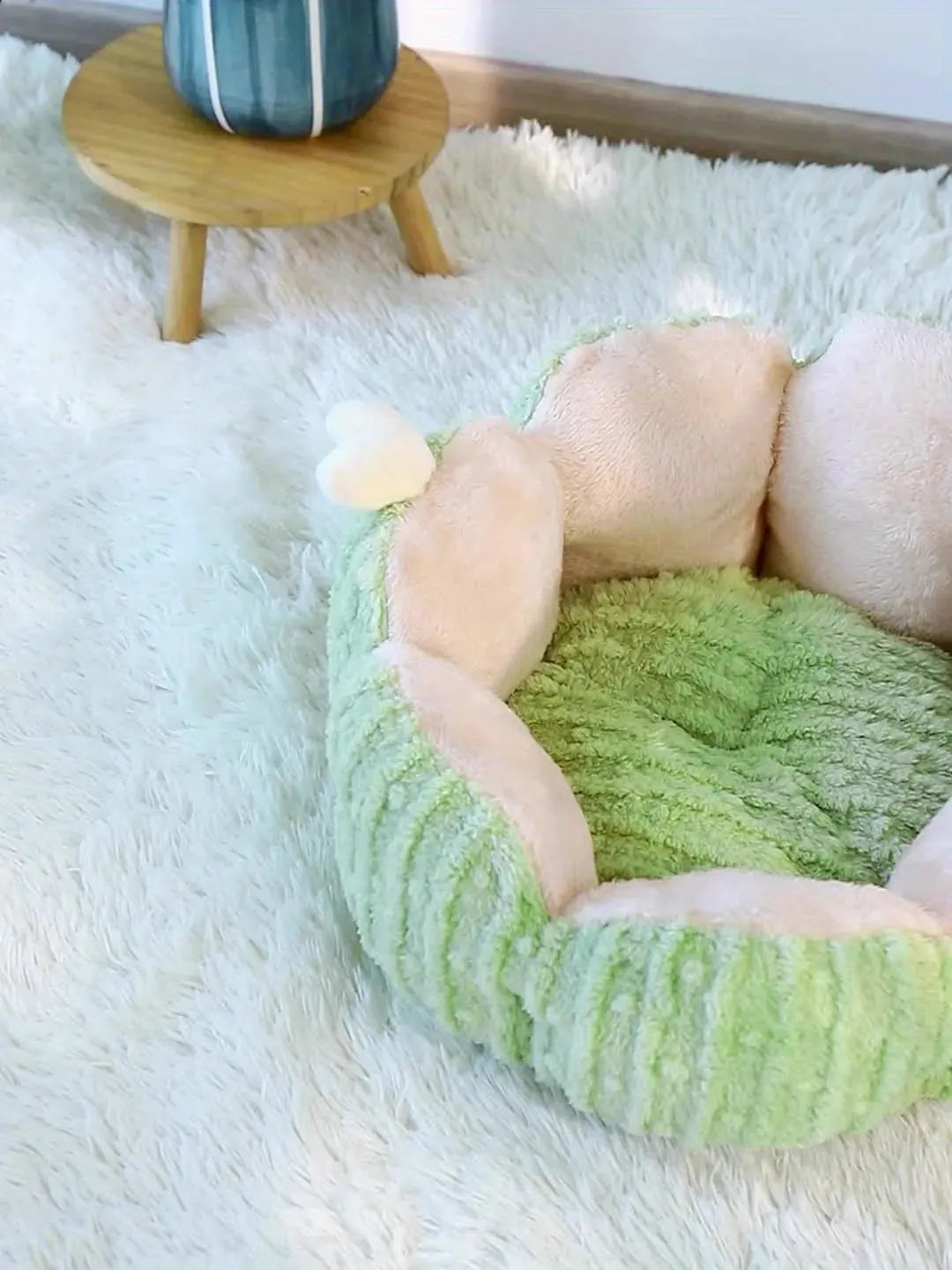 A green and pink round cat bed on a white rug, offering cozy and soft bedding for cats